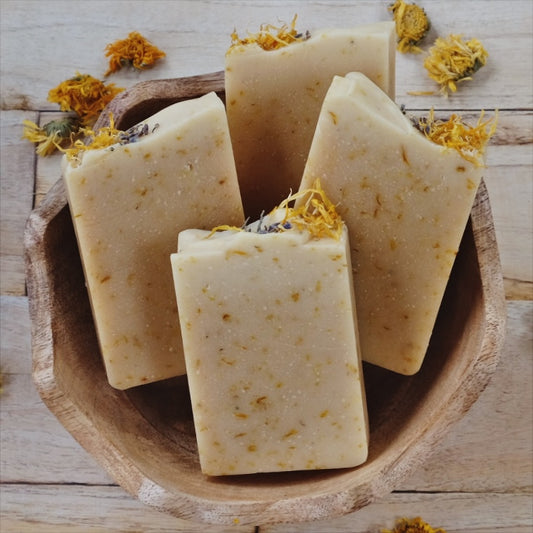 Golden Glow coconut milk soap bars laying in a wooden bowl on a wooden table. Scented with Lemongrass and lavender and naturally colored with calendula petals, colloidal oatmeal and kaolin clay.