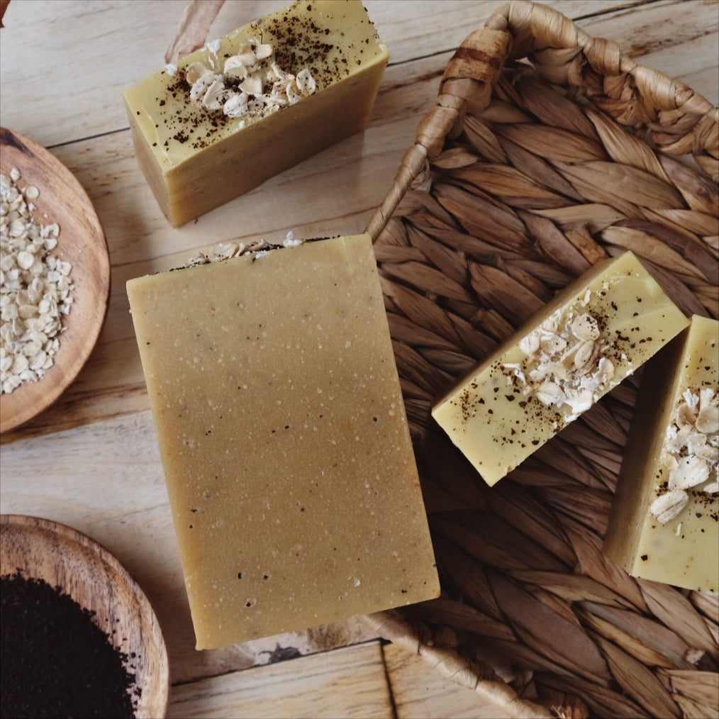Tan and speckled Atlas Brew Coconut milk soap bars laying in a brown basket, surrounded by oats and coffee beans. Naturally scented with Cedarwood Atlas and orange essential oils.