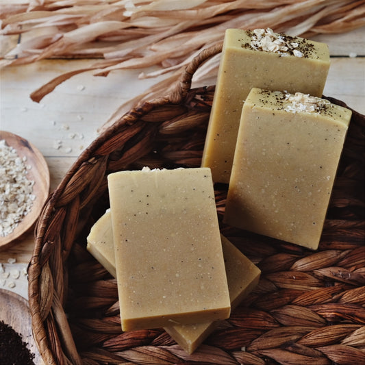Tan and speckled Atlas Brew Coconut milk soap bars laying in a brown basket, surrounded by oats and coffee beans. Naturally scented with Cedarwood Atlas and orange essential oils.