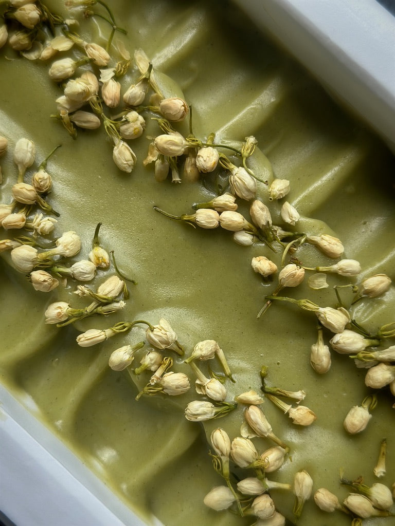 Freshly poured Green Meadow Mint coconut milk soap uncut and in the soap mold, naturally colored with organic spinach powder and Moringa leaf. Scented with a blend of peppermint and spearmint essential oils and decorated with dried jasmine flowers. 