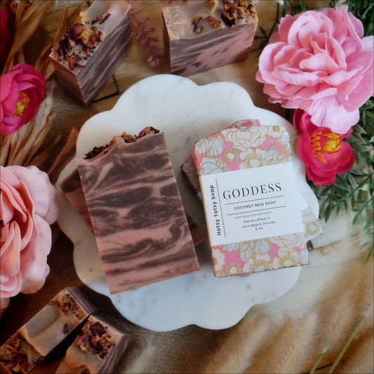 Assortment of pink and brown soaps surrounded by florals and soap bar wrapped in pink and gold packaging