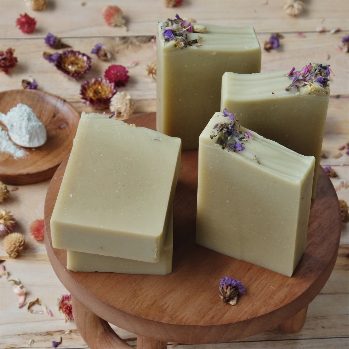 Stack of 5 green Coconut milk soaps scented with  lavender, ylang ylang, frankincense and cedarwood. atlas on a wooden stand surrounded by dried flowers.