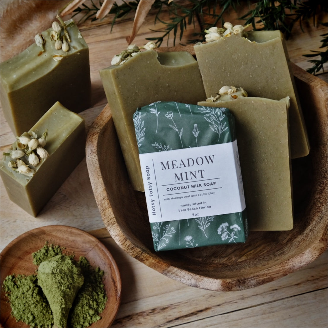 Meadow Mint coconut milk soap is naturally colored with organic spinach powder and Moringa leaf. Scented with a blend of peppermint and spearmint essential oils. Each soap is hand-wrapped in a dark green paper with a delicate white floral pattern.