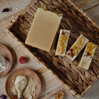 Light yellow coconut milk soap bars scented with lavender, litsea cubeba and geranium essential oils and Naturally colored with yellow clay, colloidal oatmeal and kaolin clay laying in a woven basket surrounded by botanicals.
