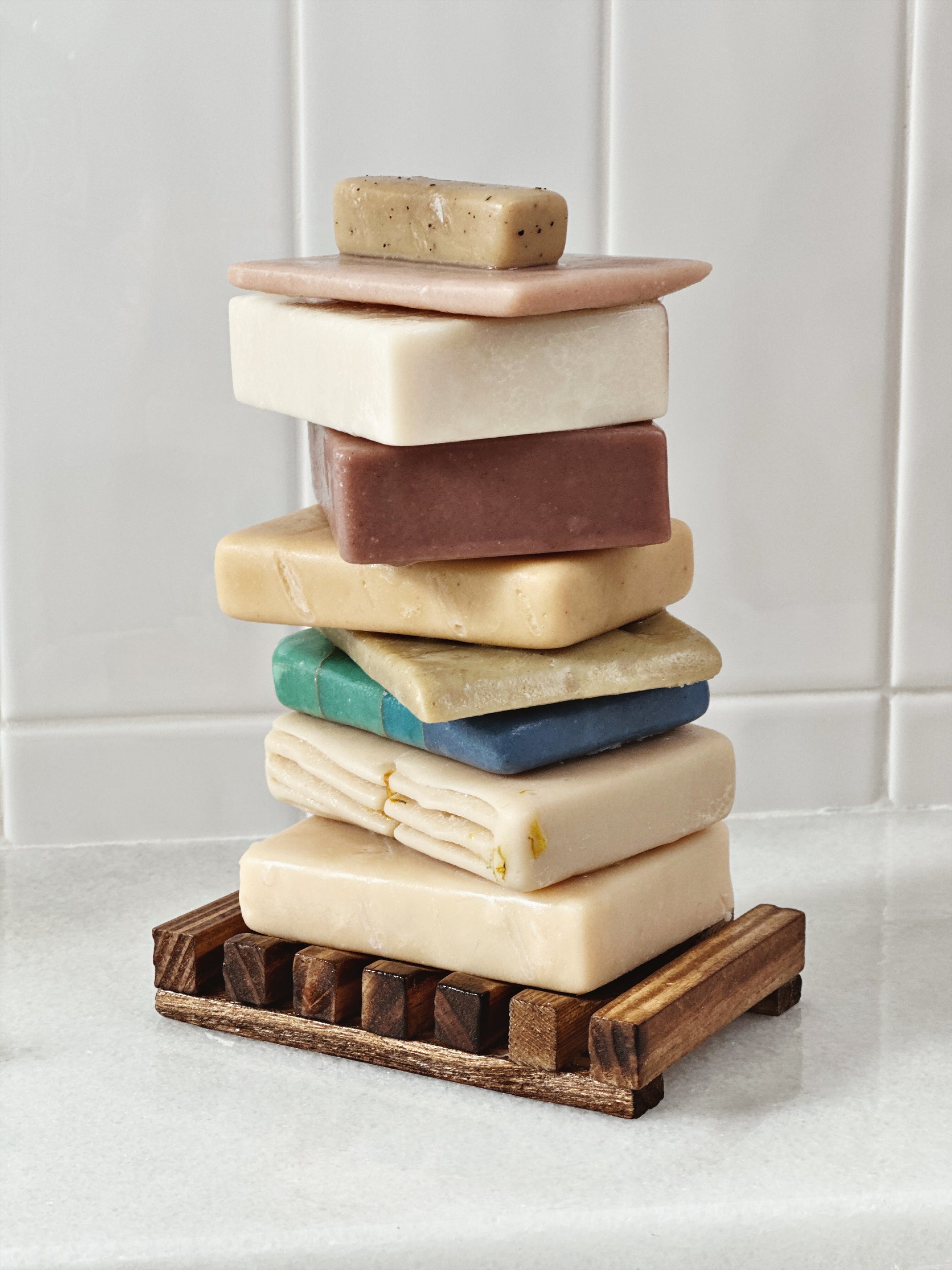 Brown bamboo slotted soap dish stacked with a variety of colored soaps 