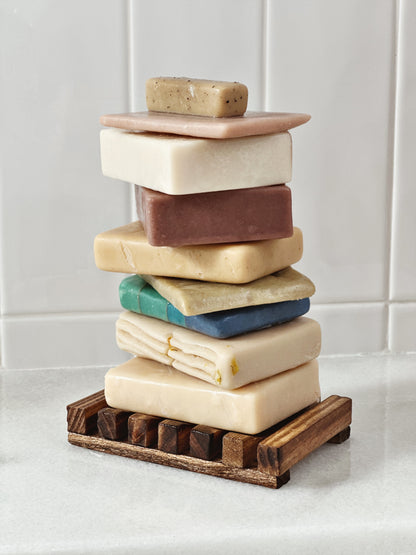 Brown bamboo slotted soap dish stacked with a variety of colored soaps 