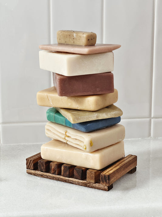 Brown bamboo slotted soap dish stacked with a variety of colored soaps 