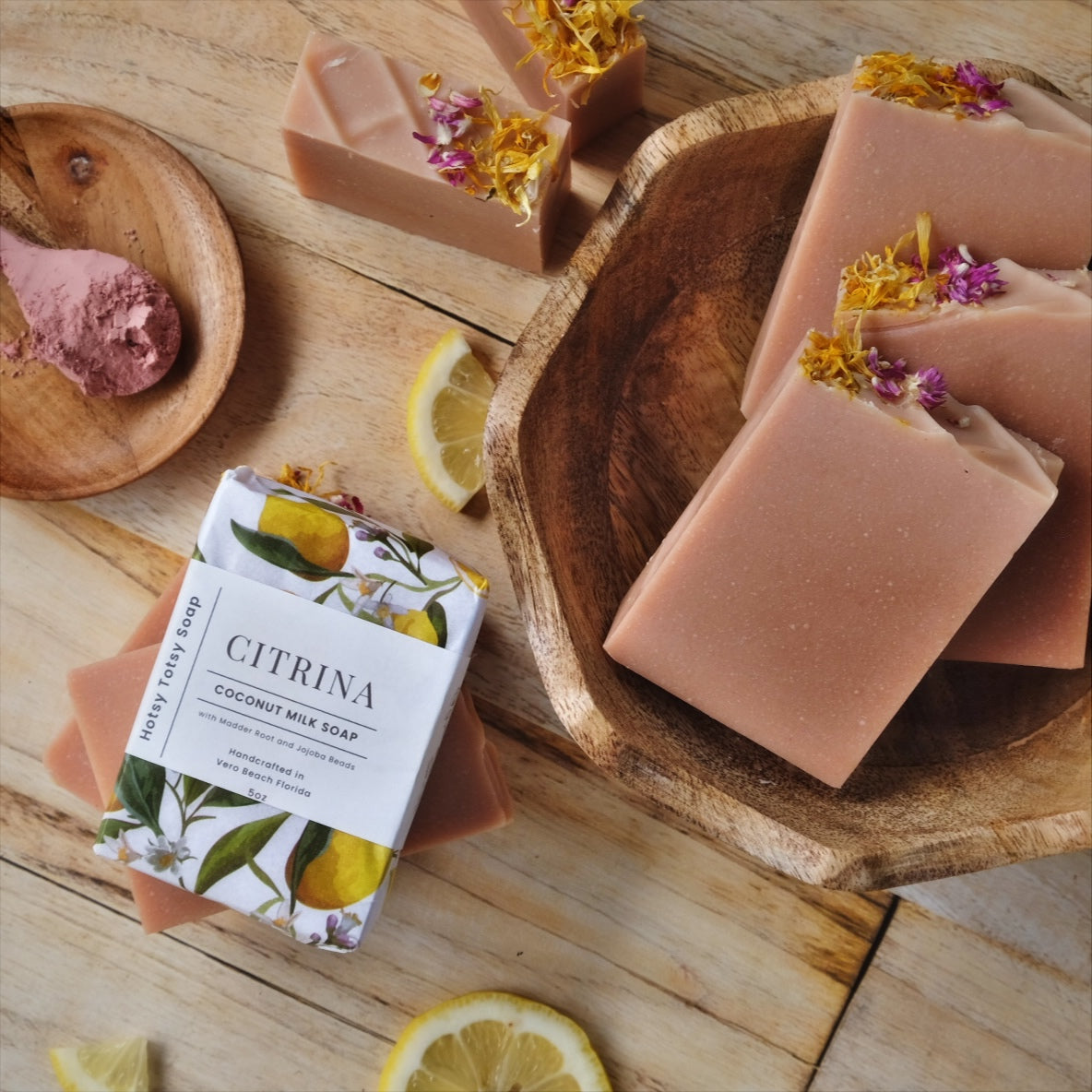 coconut milk soap bars stacked in a wooden bowel, naturally colored with French Pink clay. Scented with a blend of Bergamot, Litsea cubeba, and frankincense essential oils and decorated with dried flowers.
